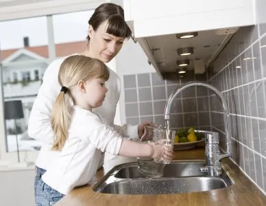 Mom helping her daughter get water from the kitchen faucet