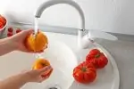 Woman washing vegetables on a white kitchen sink