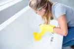 woman removing hard water stains from bathtub