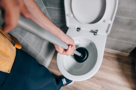 Man cleaning toilet with a plunger