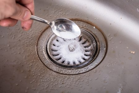 Person unclogging the sink with baking soda.