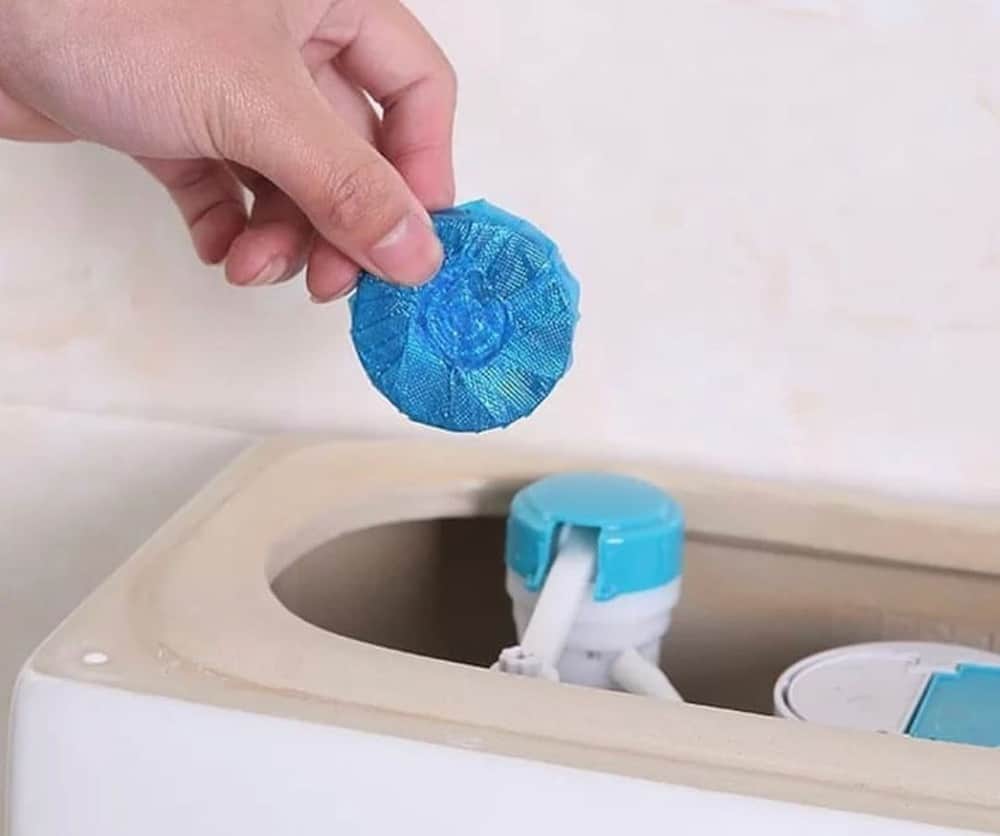 Person putting a toilet cleaner into the toilet tank