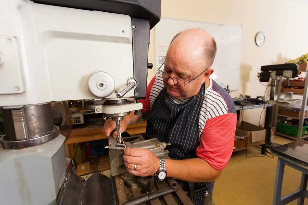 Senior male artisan working on industrial drilling press