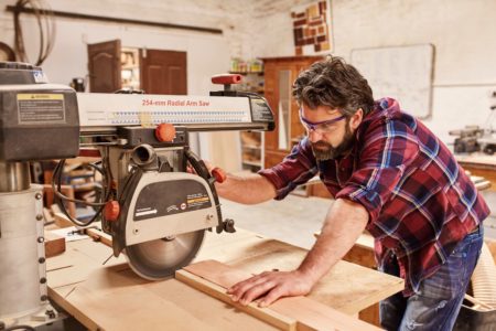 Carpenter using radial arm saw to cut wood in workshop