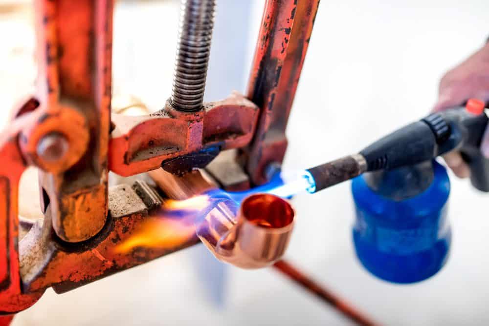 Worker using propane gas torch for soldering copper pipes.