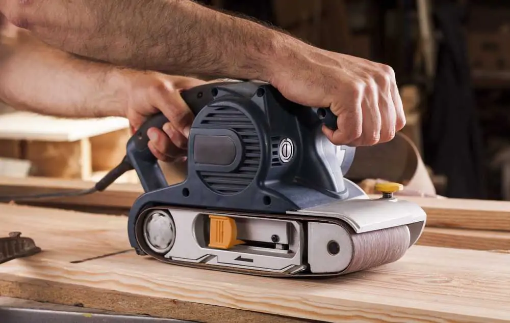 Carpenter works with belt sander for woodworking