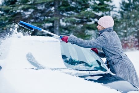 Woman removing snow from a car with a snow brush