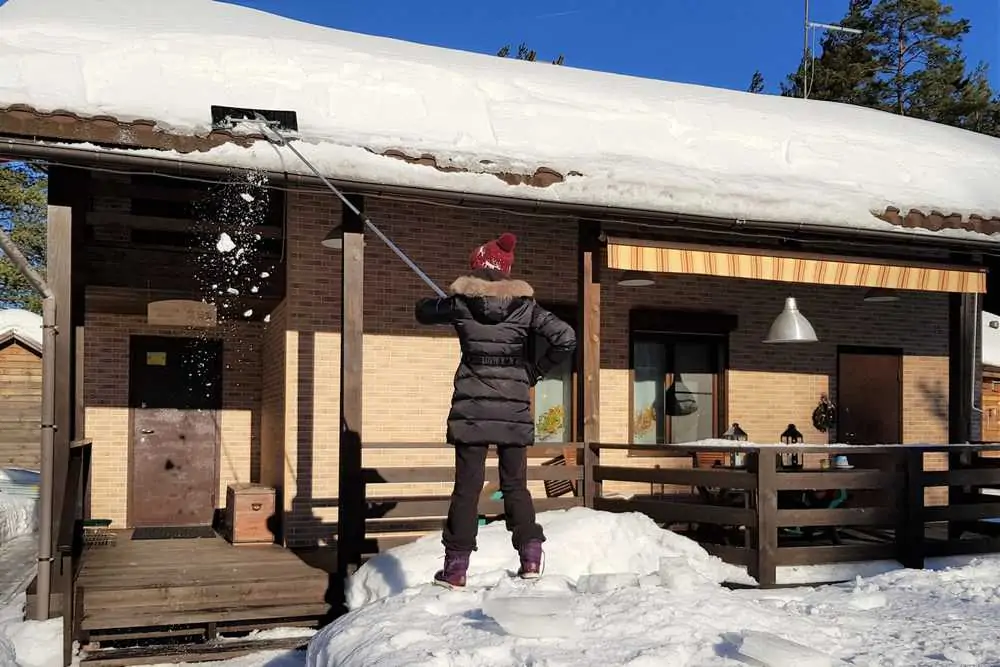 Woman cleans snow with shovel from roof of house