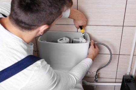 Plumber repairing toilet cistern at water closet