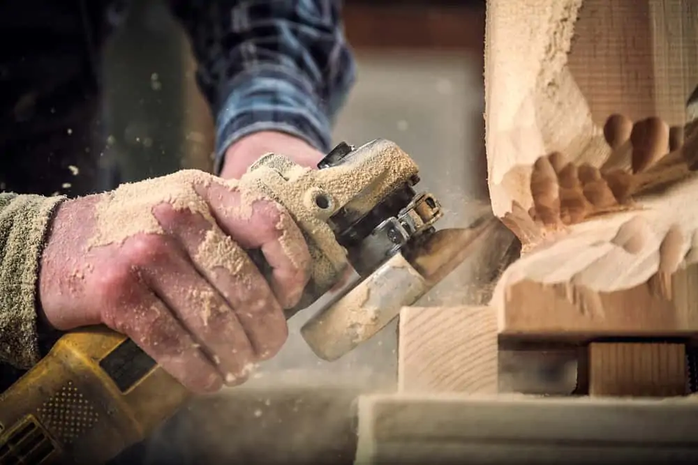 Carpenter in work clothes using angle grinder to cut wood