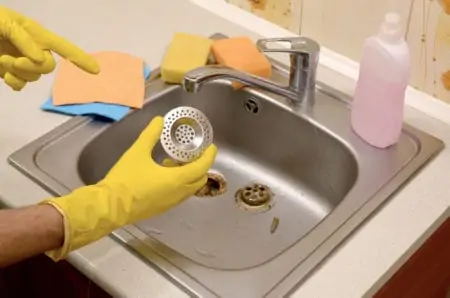 Person holding a sink stopper over a kitchen sink