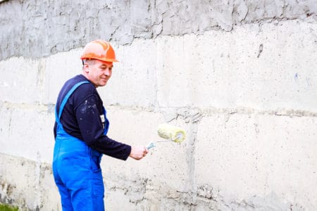 A builder with a roller painting concrete wall