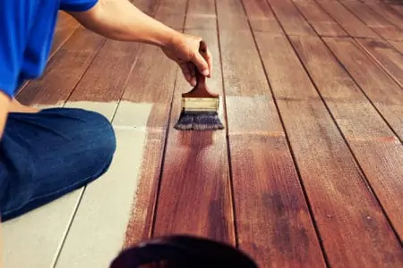 Person painting a deck with a paint brush