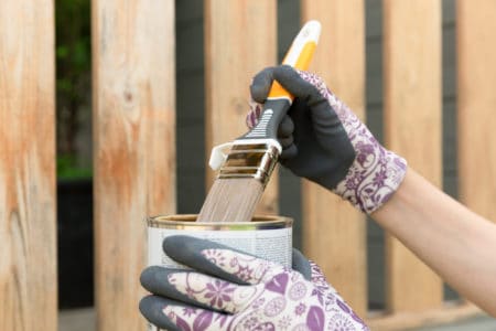 Woman's hand with a paintbrush painting a wooden fence