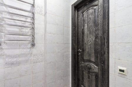 Classical closed wooden black oak door in white tiled mosaic wall of the bathroom