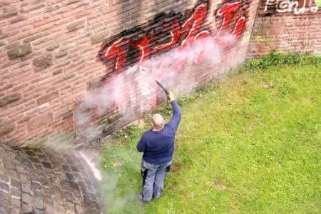 A worker washes spray paint off a wall