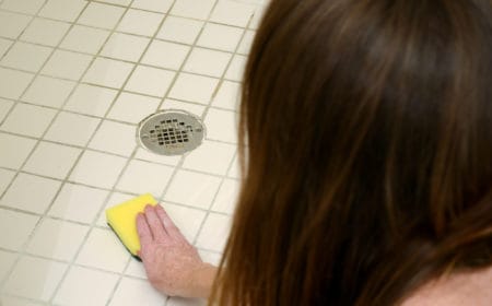 Woman scrubbing shower tiles with scour pad to clean soap scum