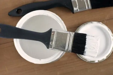 Black brush dipped in primer laying on paint cans