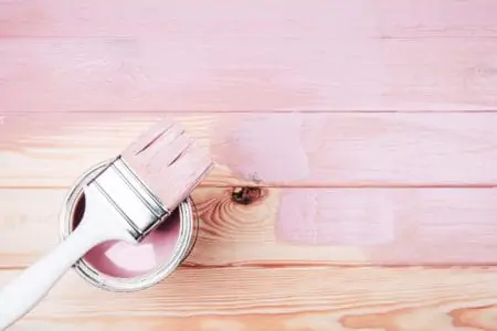 Open can of pink paint with white brush over it