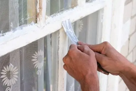 Close up male hands make putty works with putty knife. Fixing wooden window for protection, warterproof