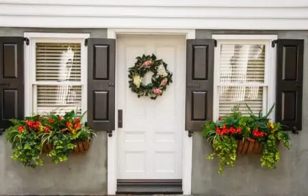A small home decorated with two window boxes with flowers and a nice home made wreath of magnolia leaves