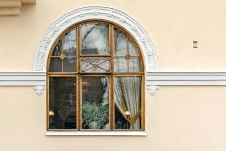 Triple arched window with a wooden frame and white stucco on the background of the wall of light beige.