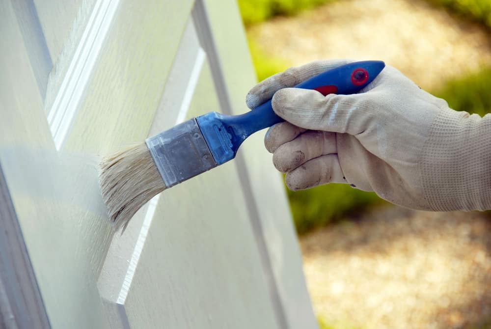 Painting wooden door in white color by blue brush