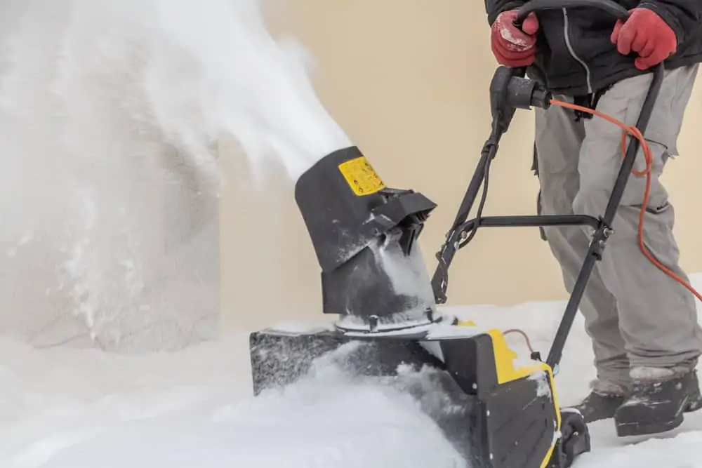 Man is brushing white snow with the yellow electric snow thrower in a winter garden