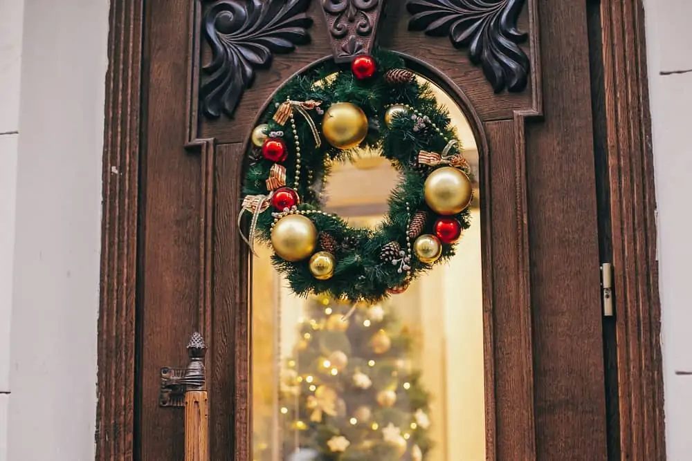 Traditional christmas wreath with red ornaments and gold baubles on old wooden door in european city street. Stylish christmas street decor, Festive decorations and illumination. Winter holidays