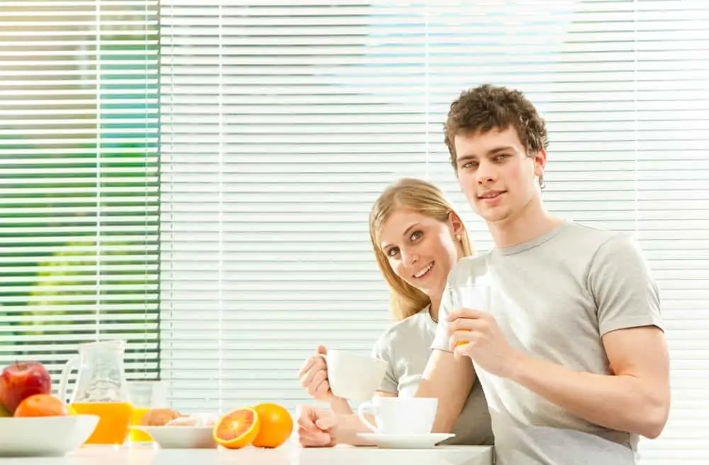 Young casual couple have breakfast with coffee and fruit with venetian blind window