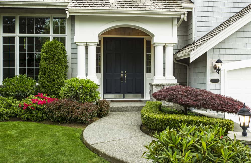 Front Door to home surrounded by seasonal plants and part yard and sidewalk in forefront