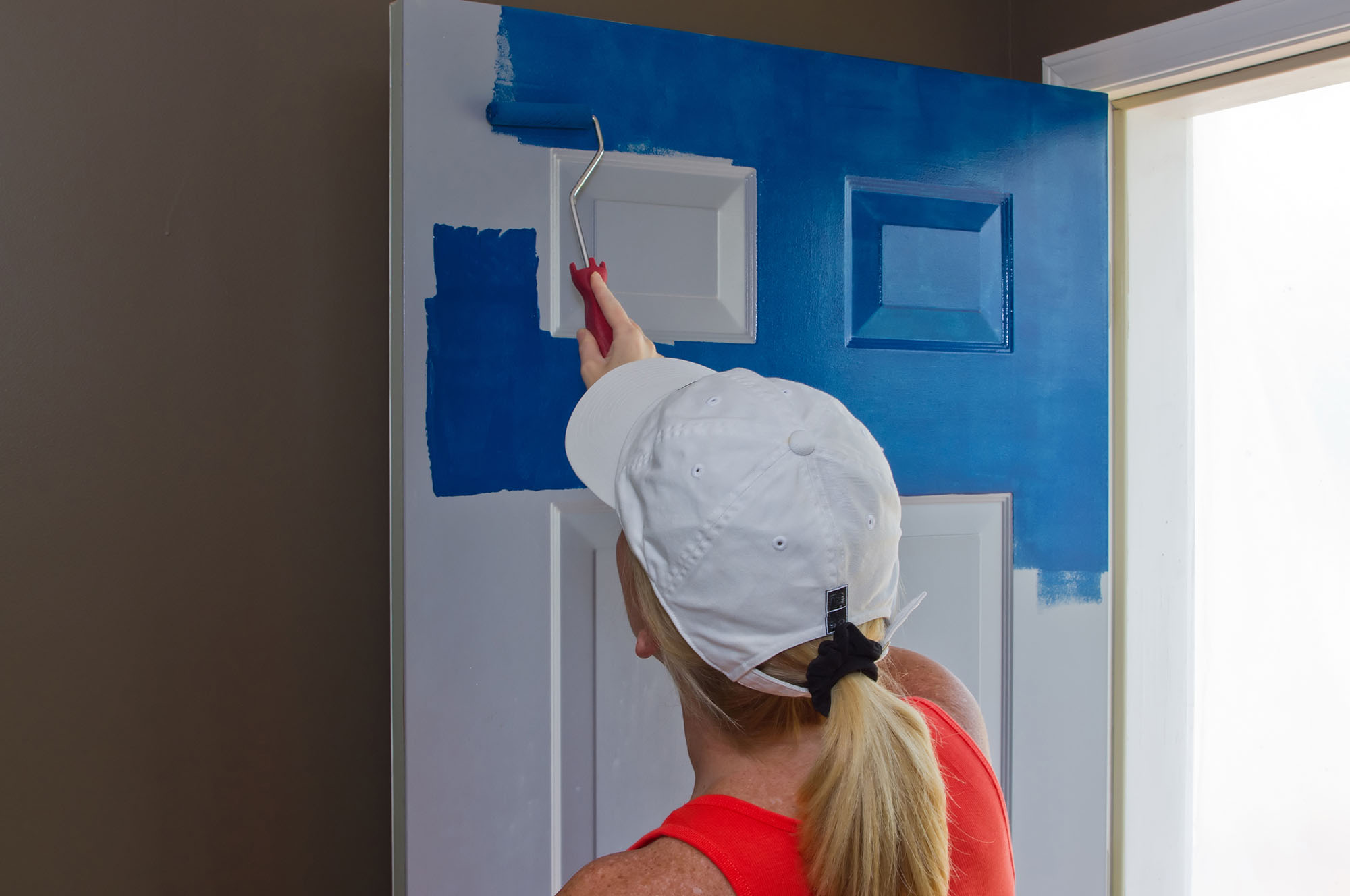 Blond Woman painting the outside of a door blue