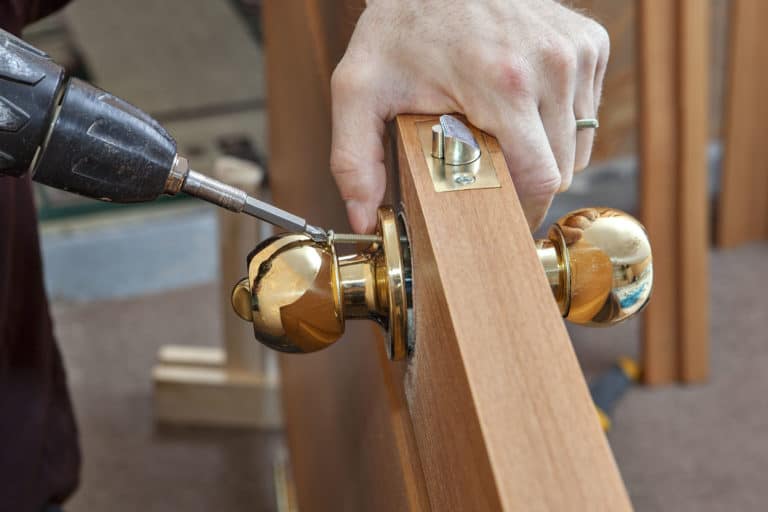 Install the door handle with a lock, Carpenter tighten the screw, using an electric drill screwdriver, close-up.