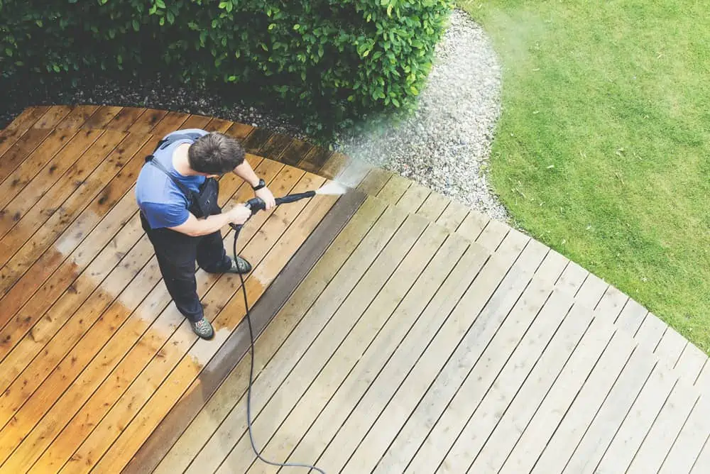 man cleaning terrace with a power washer - high water pressure cleaner on wooden terrace surface