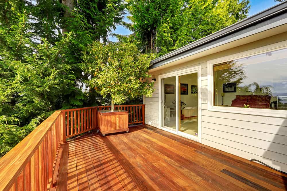 Wooden walkout deck with railings and decorated with tree.