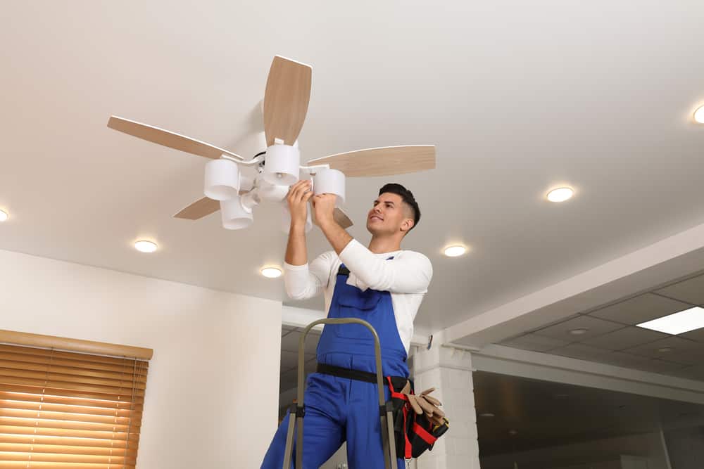 Electrician changing light bulb in ceiling fan indoors