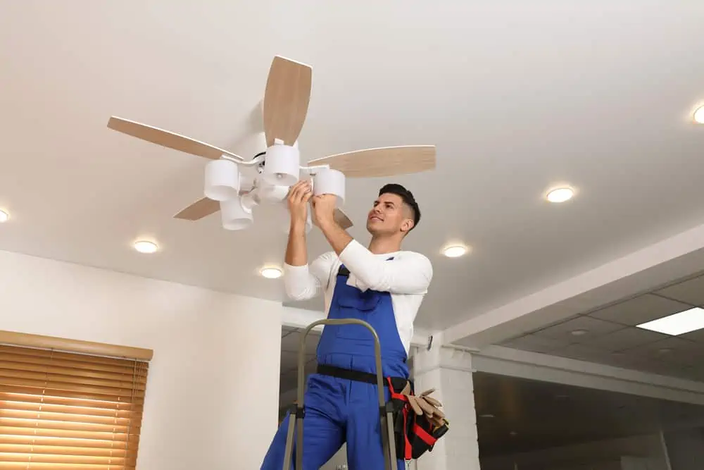 Electrician changing light bulb in ceiling fan indoors