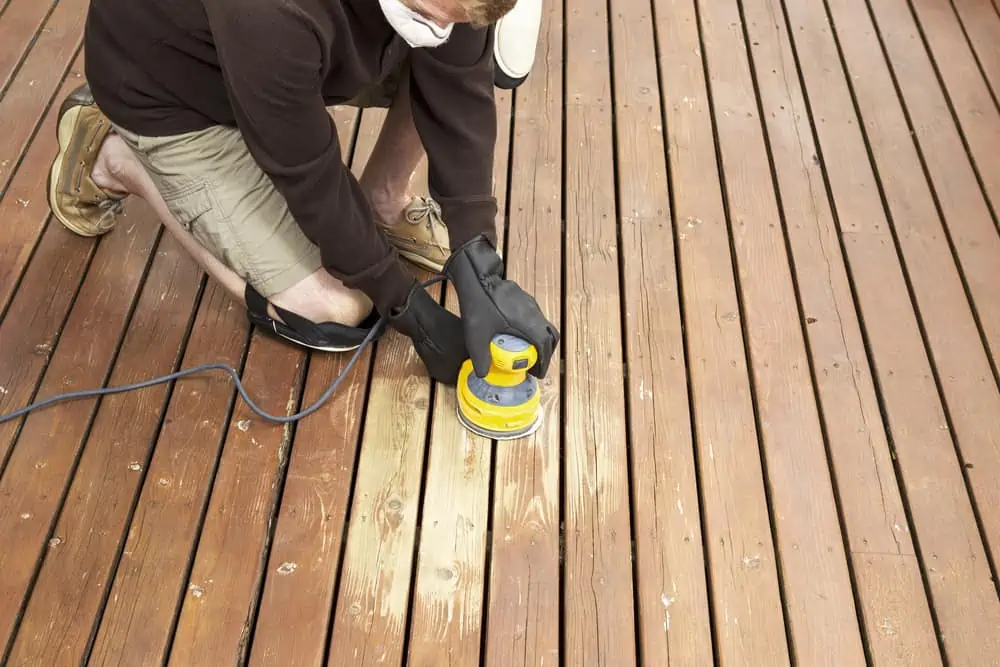 Horizontal photo of mature man kneeling while sanding outdoor wooden deck