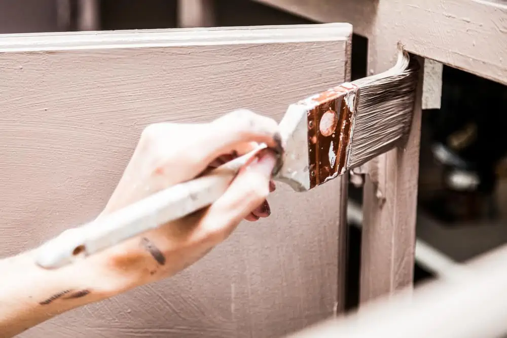 Closeup of Person Holding Paint Brush and Painting Kitchen Cabinets