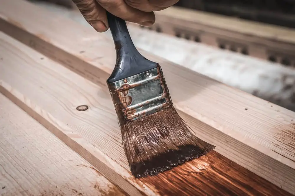 Painter with paintbrush painting wooden surface for protection wood from external influences