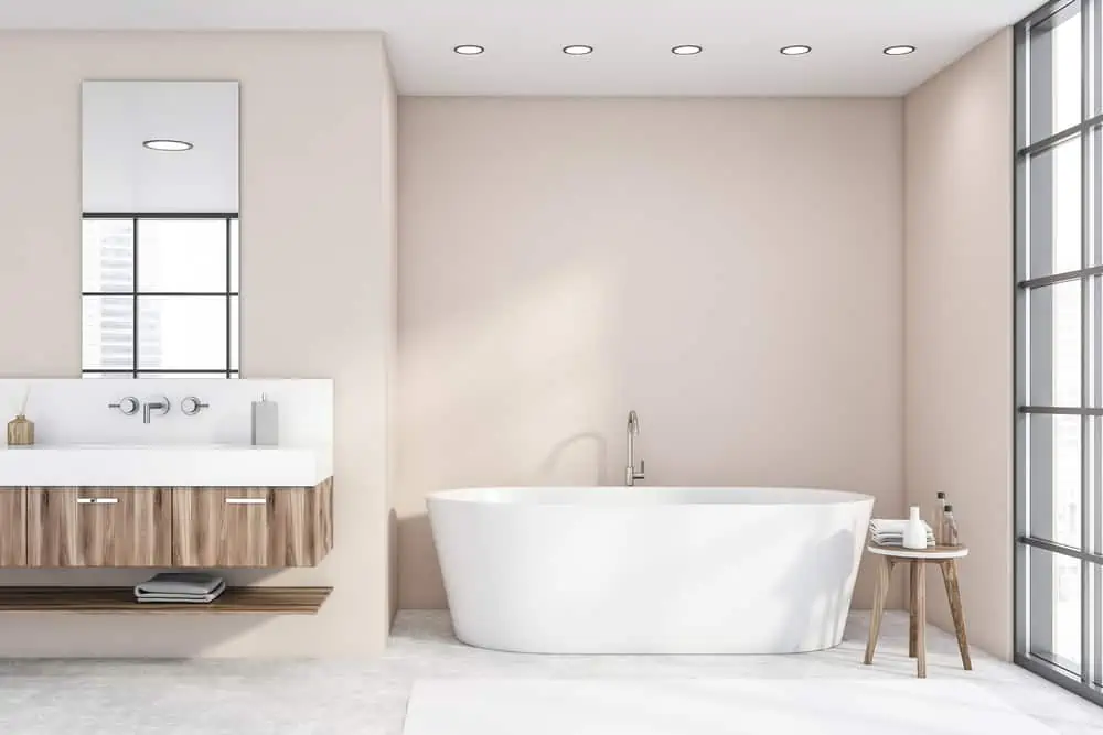 Comfortable white bathtub and sink with vertical mirror standing in stylish bathroom with beige walls and concrete floor. 3d rendering