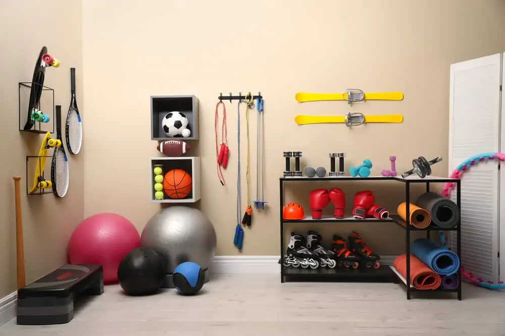 Many different sports equipment in room with beige walls