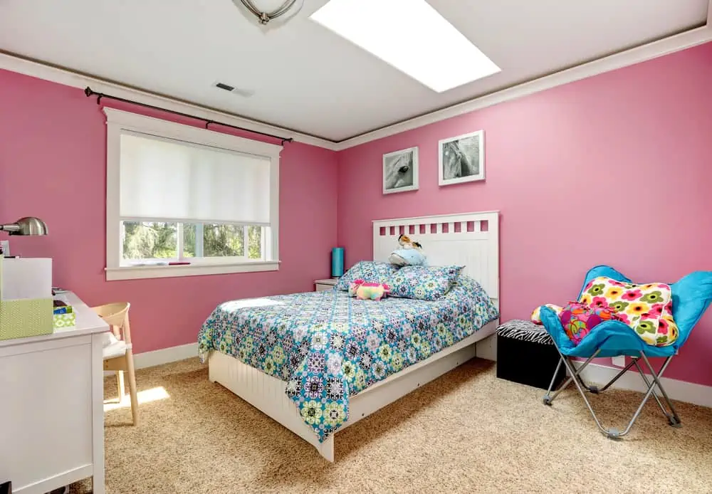 Gentle girls bedroom with white bed and pink walls. View of bed with blue bedding,blue chair