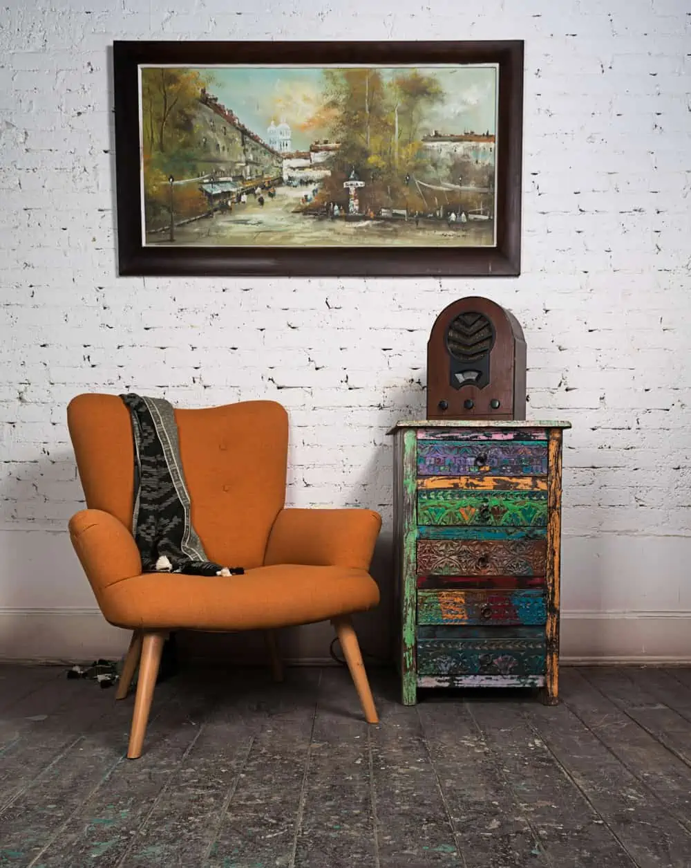 Composition of vintage orange armchair, colorful cupboard, aged wooden radio and hanged painting