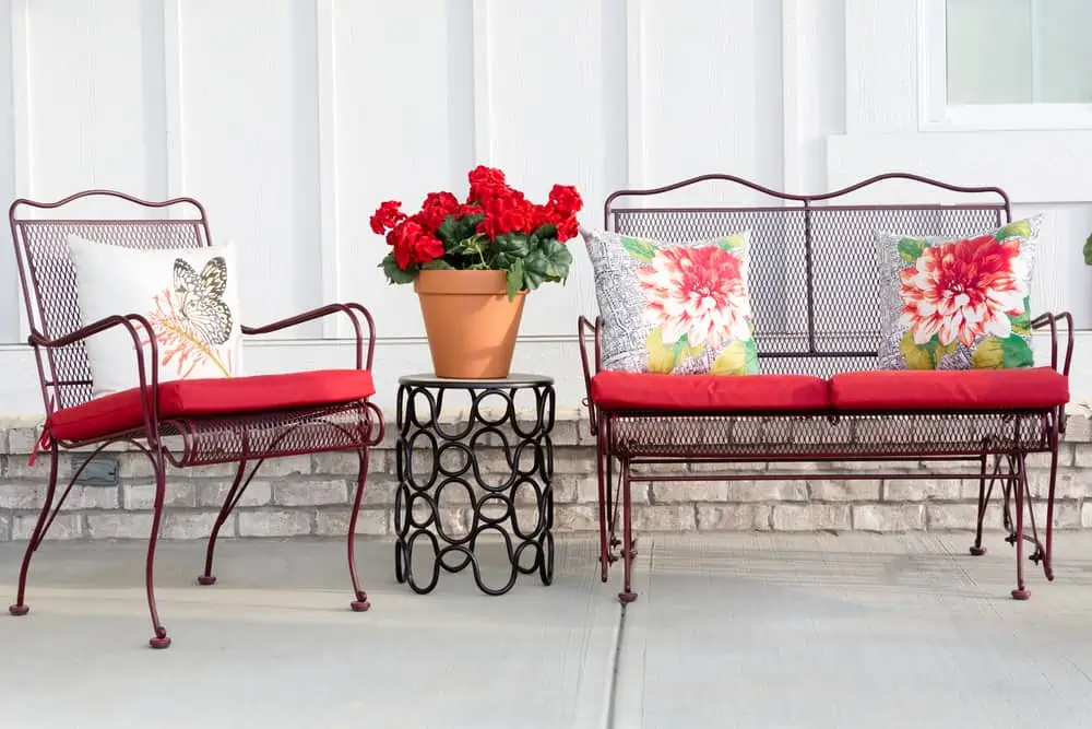 Colorful wrought iron garden furniture with vibrant red cushions and a red potted geranium standing on an open-air front patio or porch ready for the warm spring and summer weather