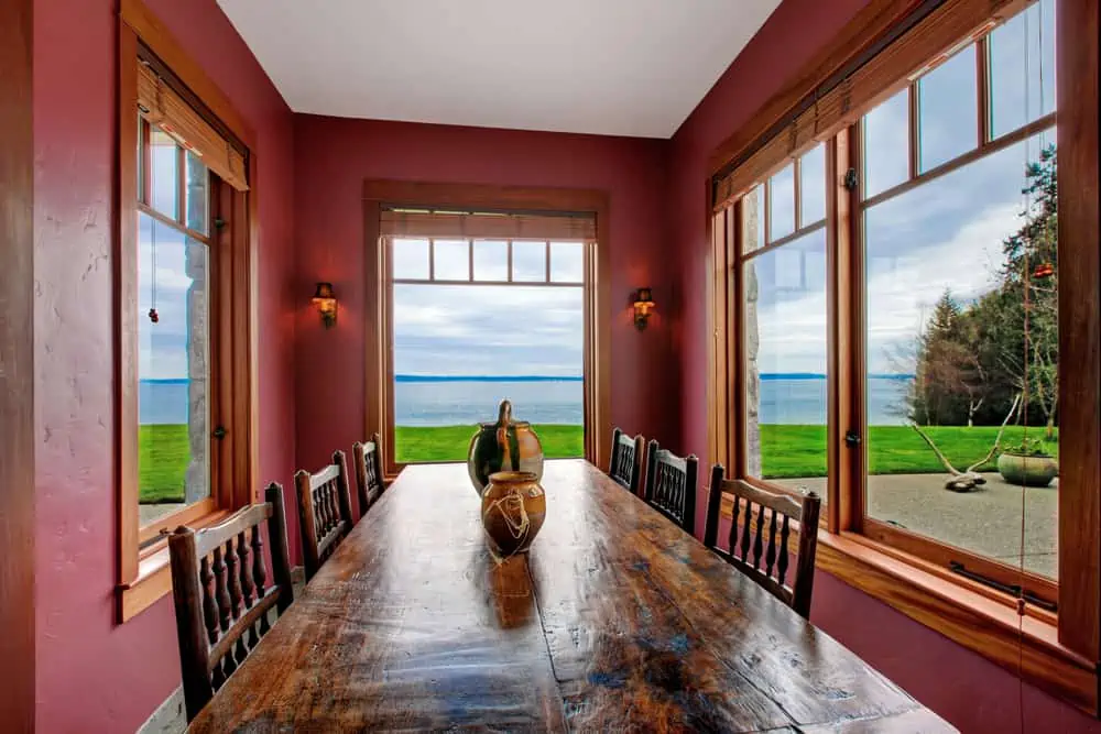 Antique style dining room with rustic table set, burgundy walls and windows