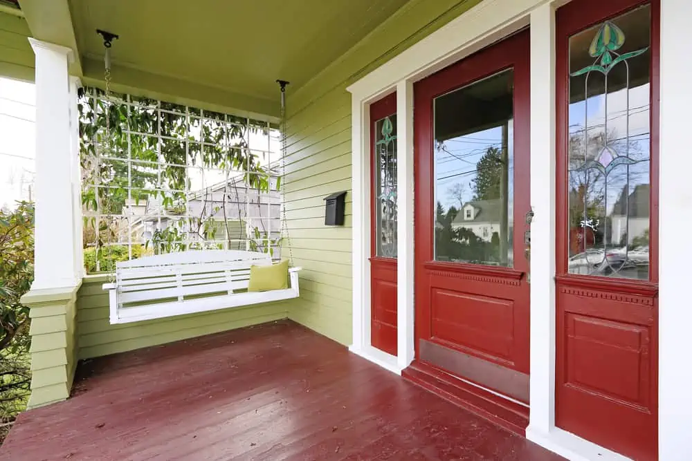 Entrance porch in old house with contrast green and red walls. View of white wooden hanging swing