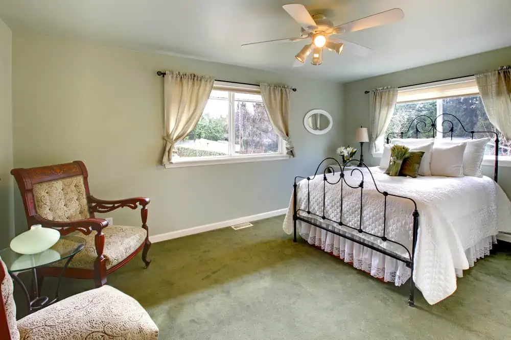 Olive tones bedroom with antique iron frame bed, green carpet and aristocratic chairs