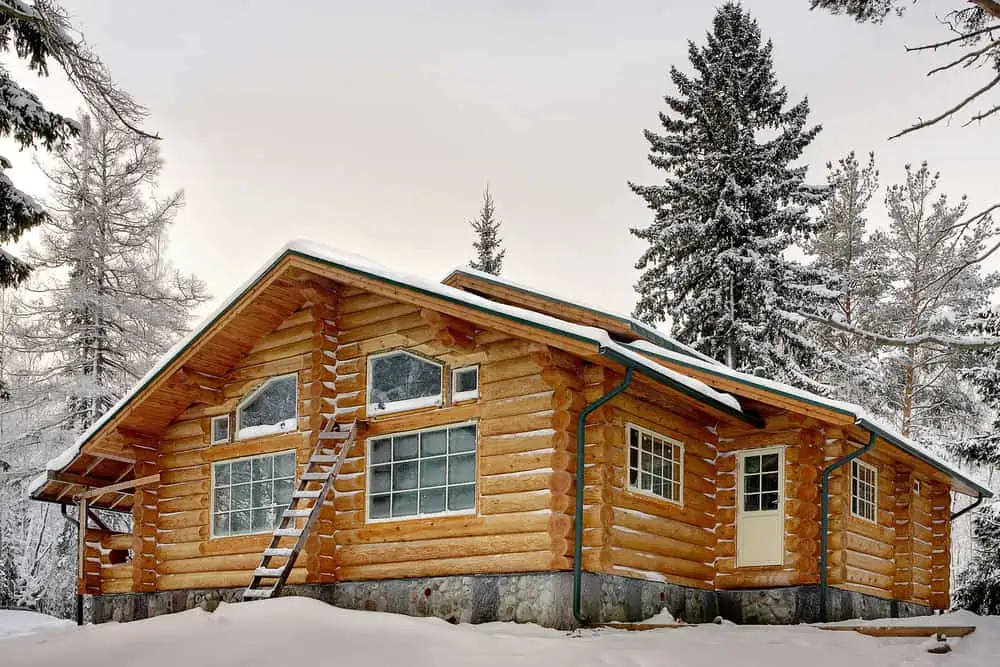 Modern handmade log house with large windows covered in snow during winter.