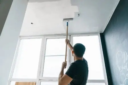 the man paints the walls and the ceiling in gray color, standing with his back to the camera. Focus on the roller. Painting and repair of the room.